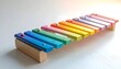 © krisna - A colorful wooden xylophone toy rests on a white surface, showcasing vibrant rainbow hues and simple design, evoking childhood joy and musical discovery