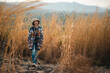 © chokniti - Woman traveler wearing colorful patterned sweater and hat standing in golden grass field under warm sunlight enjoying nature, outdoor adventure, and peaceful autumn atmosphere at countryside