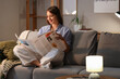 © Pixel-Shot - Young woman reading newspaper on sofa at home in evening