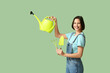© Pixel-Shot - Beautiful young woman with watering can, rake and shovel on green background