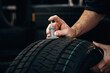 © standret - Hand of a technician measuring tire tread depth with a gauge on a black tire in a workshop surrounded by additional tires in the background