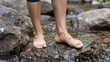 © Nopadol - Barefoot Solitude: A serene moment captured as bare feet find their balance on a stone, a tranquil escape amidst a flowing stream, evoking a sense of connection with nature.