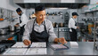 © Alfin - Chef reviewing recipes on tablet in a commercial kitchen with kitchen staff working in the background