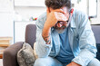 © simona - Sad and frustrated 50s man suffering from stress, depression at home, sitting on sofa, touching head, feeling headache, migraine, dealing with loss, grief, trauma. Nervous breakdown, crisis concept