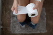 © kieferpix - Woman holding toilet paper roll while sitting on toilet in bathroom