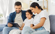 © Studio Romantic - Happy family parents and child at home. Smiling daughter on couch with mother and father using tablet together. Warm living room shows trust, care, and unity. Technology and loving family time.