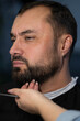 © Liudmila - Barber trimming beard of adult man with straight razor in barbershop. Close-up of professional male grooming and beard care, hairstylist shaping beard during haircut service in modern salon.