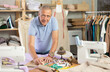 © JackF - Mature male tailor stands near a table in the workshop and makes markings for patterns on paper. Fashion designer plans to sew a collection of clothes