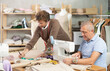 © JackF - Elderly man tailor sews on machine adult man assistant drawing pattern on paper in workshop