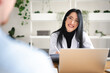 © Studio Marmellata - A smiling woman in a white coat and glasses is working on a laptop and tablet, interacting with a patient in a bright, modern office setting.