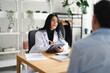 © Studio Marmellata - A doctor in a white coat consults with a patient, taking notes on a tablet in a modern office setting.