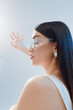 © SHOTPRIME STUDIO - Profile of a beautiful woman with long dark hair wearing clear glasses and white top, reaching out with her hand towards bright light. Concept of beauty, fashion, and elegance.