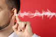 © New Africa - Hearing health. Man with audio waves coming to his ear on red background, closeup