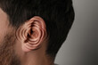 © New Africa - Hearing health. Man with audio waves around his ear on grey background, closeup