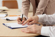 © Pixel-Shot - Business mediator with client writing in clipboard on table, closeup