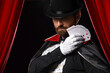 © Pixel-Shot - Male magician with playing cards near red curtains on dark background