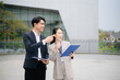 © laddawan - Asian business professionals discussing documents outdoors, showcasing teamwork, corporate strategy, leadership and modern workplace collaboration