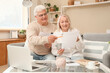© Pixel-Shot - Senior couple with refund forms and money sitting on sofa at home