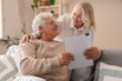 © Pixel-Shot - Senior woman hugging her husband with refund form at home