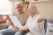 © Pixel-Shot - Senior couple with refund form sitting on sofa at home
