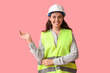 © Pixel-Shot - Young female construction worker showing something on pink background. Woman in male profession concept