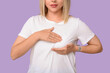 © Pixel-Shot - Young woman checking her breast on lilac background. Cancer awareness concept