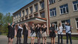 © Довидович Михаил - Energetic teens joyfully waving and celebrating the conclusion of the school year outside their high school