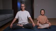© Aliaksandr - Mother and daughter sit cross legged on a yoga mat in the living room, eyes closed and hands resting on knees as they practice evening mindfulness and peaceful bonding together
