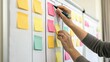 © ng-TDRD - Person organizing colorful sticky notes on a whiteboard, planning or brainstorming ideas in a collaborative or office setting.