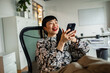 © Marko Geber - Smiling businesswoman using smartphone in modern office