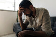 © kleberpicui - Man sitting on a sofa with a worried expression and hand on his head, portraying stress, anxiety, mental fatigue and emotional pressure in everyday life.