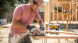 © PURPLE VISION STUDIO - Focused young adult carpenter cutting wood with circular saw at construction site. skilled worker building new home with power tool and safety equipment