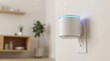 © Alexey - White cylindrical smart speaker with blue light plugged into an electrical outlet. Modern intelligent home automation device for smart living.