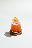 Refreshing Orange Drink with Dehydrated Citrus Garnish on Wooden Coaster.