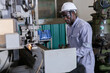 © eakgrungenerd - Industrial technician adjusting CNC milling machine in factory workshop. Engineer wearing hard hat, safety glasses and gloves ensures precision manufacturing, quality control, workplace safety.