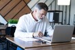© opolja - Smiling mature business man executive wearing shirt sitting at desk using laptop. Happy busy professional middle aged businessman investor working on computer looking away in office