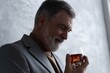 © opolja - Confident mature businessman chilling relaxing drinking enjoying whiskey against grey wall.