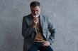© opolja - Confident mature businessman chilling relaxing drinking enjoying whiskey against grey wall.