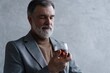 © opolja - Confident mature businessman chilling relaxing drinking enjoying whiskey against grey wall.