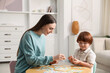 © New Africa - Mother and her son playing with toys at wooden table indoors