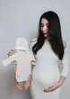 © Nataliya - A vertical hip-length portrait of a pregnant Caucasian woman holding a baby kit.