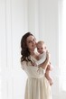 © New Africa - Smiling mother in dress holding her cute baby near white wall at home