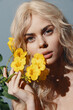 © VICHIZH - Beautiful young woman with long blonde hair holding yellow flowers, showcasing natural beauty and elegance in a soft pastel background.
