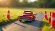 © Vadym - Red toy pickup truck navigates a miniature road course marked by orange cones and barriers. The vintage vehicle drives on asphalt path with grass and trees in soft focus background.