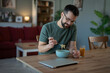 © Jelena - Man eating casual lunch at home looking at laptop