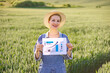 © sofiko14 - A smiling woman in a straw hat and overalls holds a paper with a growing bar chart and arrow in a field of green crops