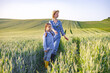 © sofiko14 - A woman and a young girl walk hand-in-hand through a lush green wheat field under a clear sky, enjoying a sunny day outdoors