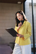 © crizzystudio - Young asian professional woman thoughtfully reviewing document on clipboard