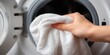 © NovaVision - Close-up of a hand placing a white towel into an open washing machine drum