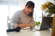 © Cristina Garcia - Woman freelancer writing notes during online work at home